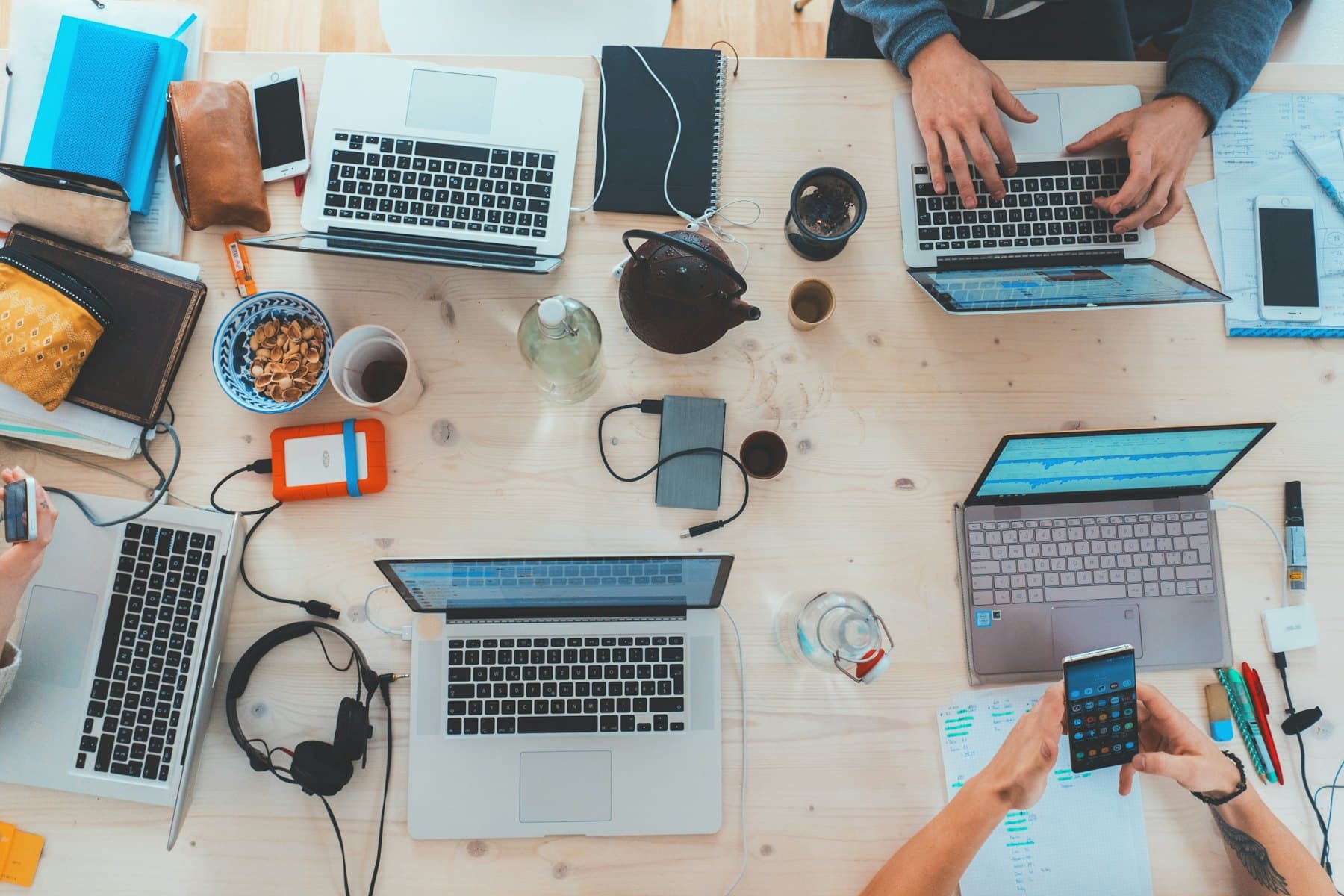 Overhead view of a desk covered in open laptops, notebooks, phones and cables.