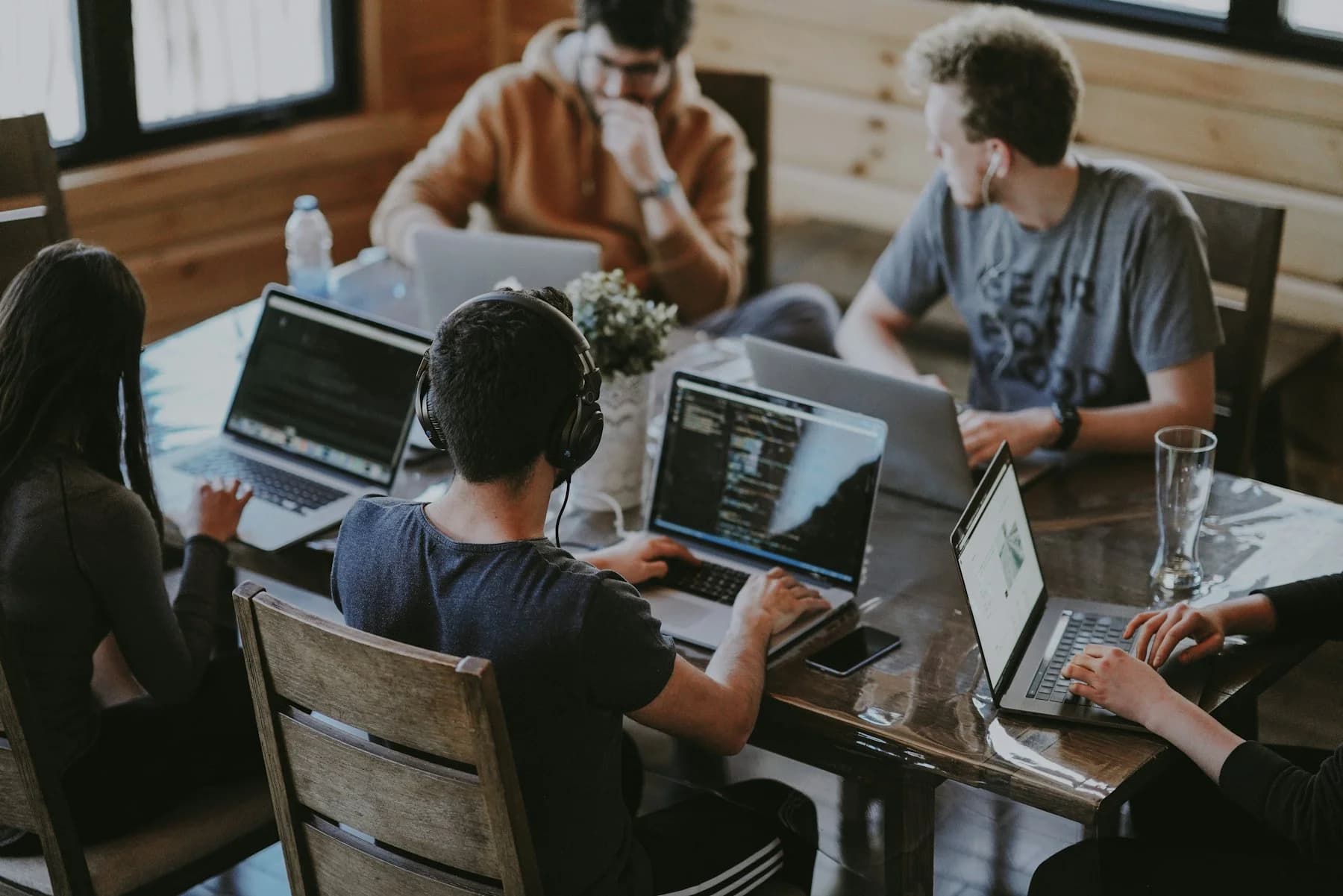 Four people working side by side on laptops at a shared table.